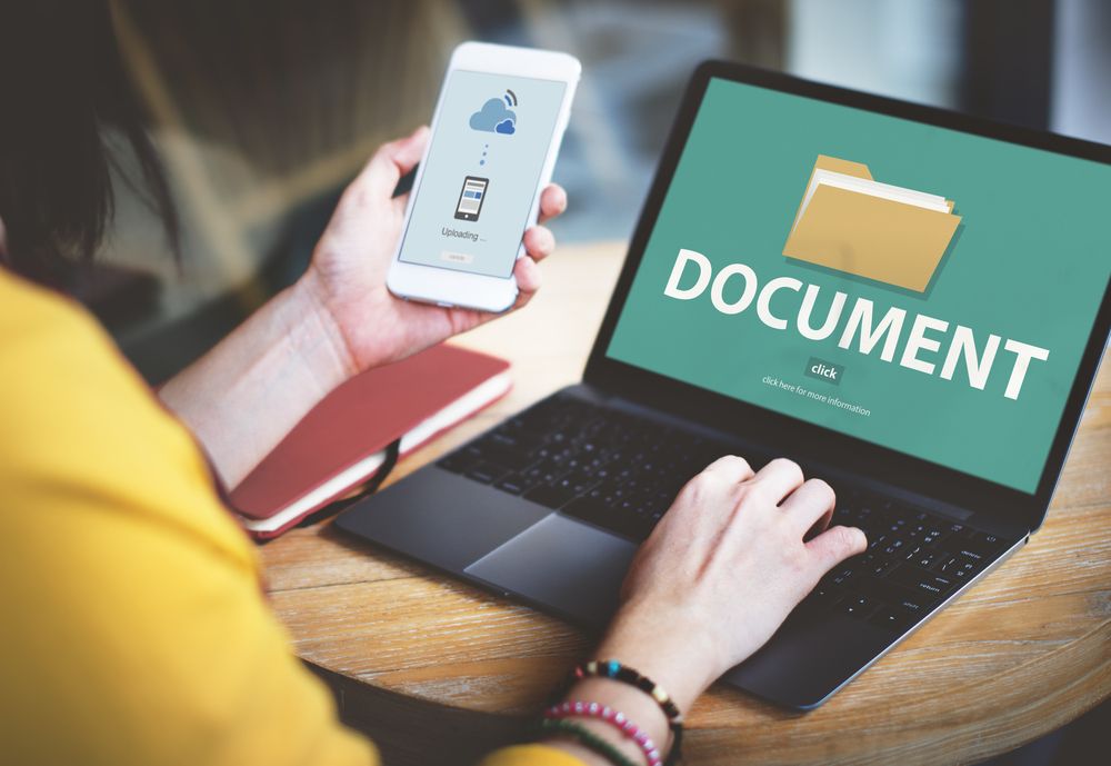  A person using a laptop and a smartphone to share files between devices with the text 'Document' on the laptop screen.